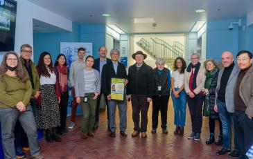 A group PMB and Rausser College students, faculty, and staff pose for a photo in the center of the Koshland Hall lobby.