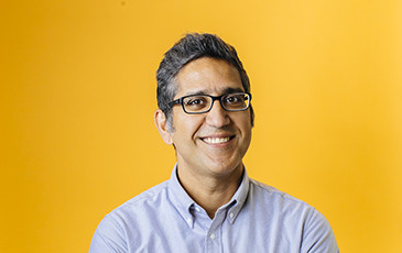 Arash Komeili smiling in front of a yellow background.